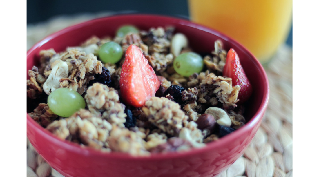 A red bowl of muesli with green grapes and strawberries